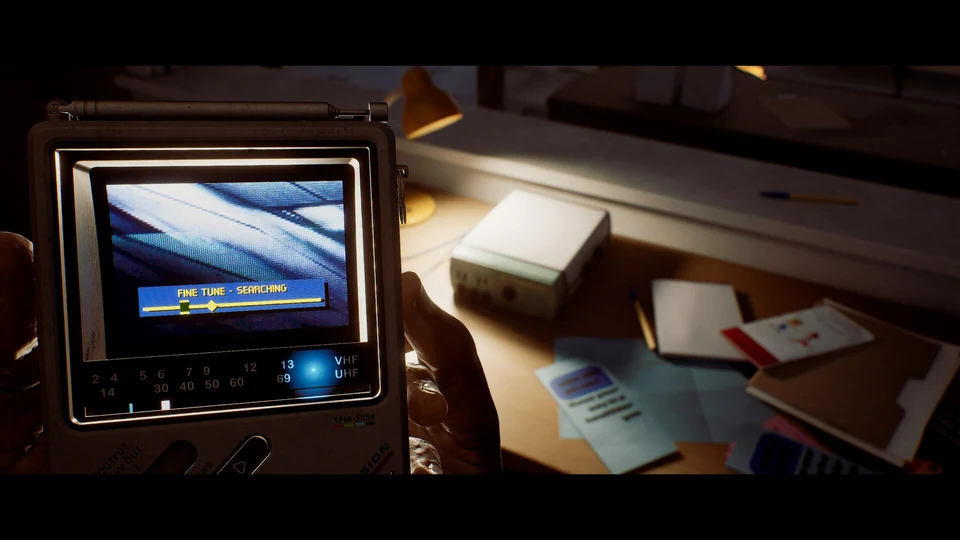 A CRTV showing a fine-tuning signal bar beside a desk covered with papers