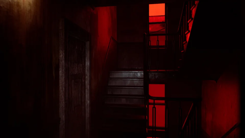 A dark stairwell with red light shining through a window and across the railings