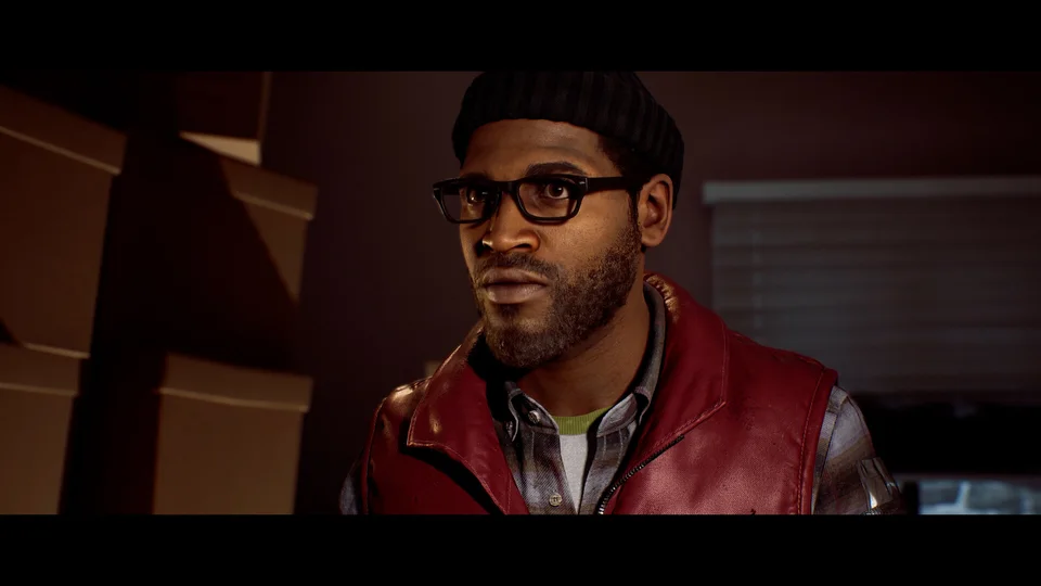 Simon in a red vest and glasses inside a room, with black bars above and below